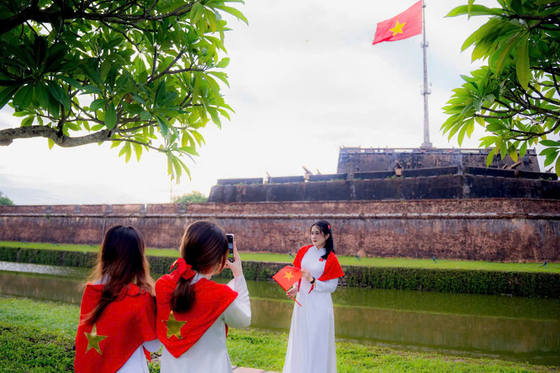 Với áo dài trắng, cờ Tổ quốc trên vai, tay - giới trẻ "check in" trước cột cờ Huế mừng 80 năm ngày Quốc khánh. Ảnh: L. Hoàng