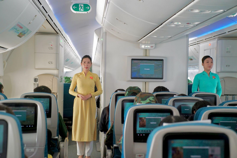 Trên chuyến bay, các tiếp viên của Vietnam Airlines cài huy hiệu cờ đỏ sao vàng trên ngực áo, mang theo sắc màu Tổ quốc trong không gian khoang bay. Hình ảnh ấy hòa chung vào không khí trang trọng của hành trình, như một lời cảm ơn gửi đến các chiến sĩ đã hoàn thành xuất sắc nhiệm vụ và trở về trong niềm tự hào.