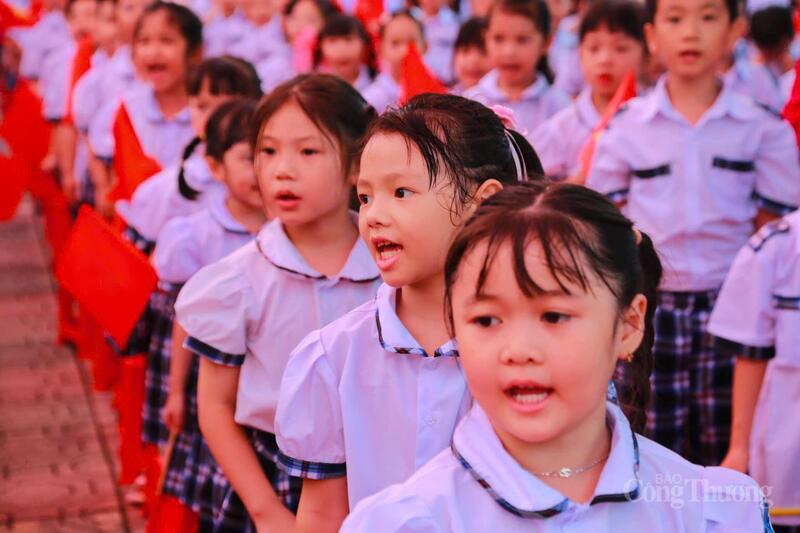 Học sinh Trường Tiểu học Xuân Đỉnh trong bộ đồng phục trắng tinh khôi, tay cầm cờ đỏ, hào hứng hát vang Quốc ca trong lễ khai giảng đặc biệt