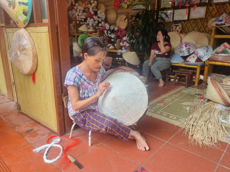 Chị Lê Thị Oanh – thợ khâu nón lâu năm tại gian hàng của nghệ nhân Lê Văn Tuy (Trung tâm sáng tạo OCOP làng Chuông) tỉ mỉ từng đường kim, giới thiệu cho du khách về quy trình làm nón truyền thống.
