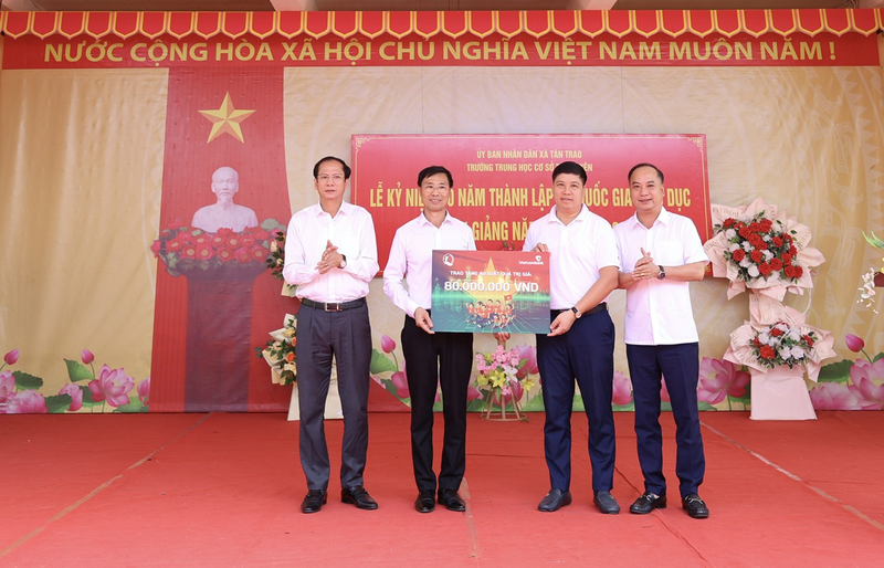 Ông Đinh Tiến Hải, Giám đốc Quỹ bảo trợ trẻ em Việt Nam (ngoài cùng bên phải) và ông Hồng Quang, Thành viên HĐQT, Chủ tịch Công đoàn Vietcombank (thứ 2 từ phải sang) trao biển tượng trưng 80 suất học bổng cho 6 trường trên địa bàn xã Tân Trào, tỉnh Tuyên Quang