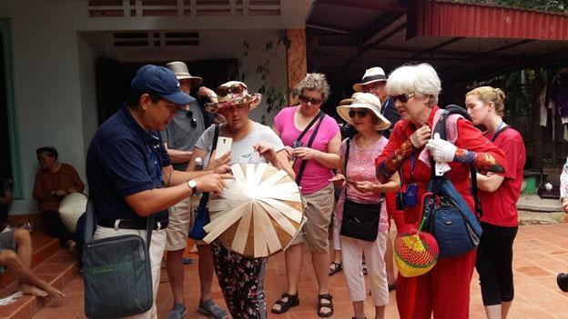 Du khách nước ngoài nghe hướng dẫn viên giới thiệu về sản phẩm nón lá Gia Thanh. Ảnh: Bình Nguyên