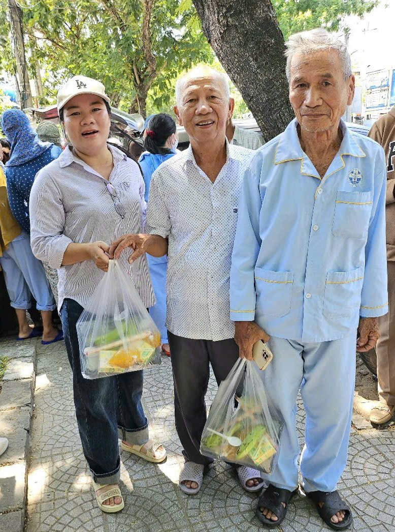 Chị Trần Thị Quy (bên trái) vui vẻ phát những suất cơm nghĩa tình cho những người già đang nằm viện. Ảnh: Nguyễn Tuấn