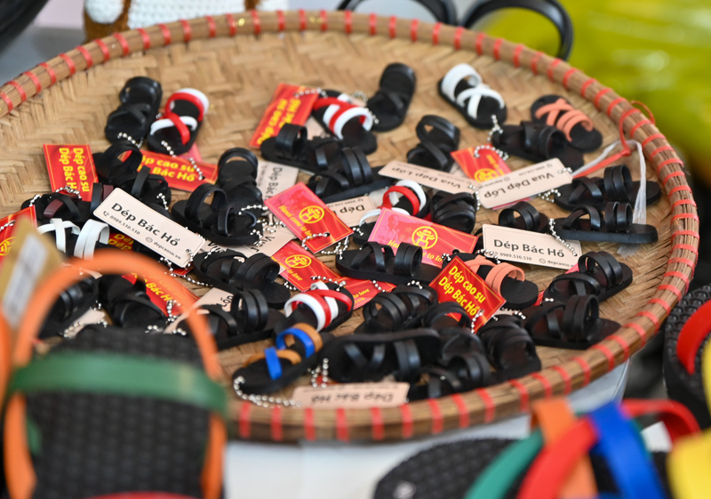 Những chiếc móc khóa mini hình đôi dép cao su được sắp xếp trên chiếc mẹt tre mộc mạc, gợi nhớ hình ảnh lao động giản dị của người Việt. Đây là sản phẩm lưu niệm được yêu thích, mang biểu tượng “Dép Bác Hồ” - biểu trưng cho sự tiết kiệm, sáng tạo và tinh thần Việt Nam thời kháng chiến.