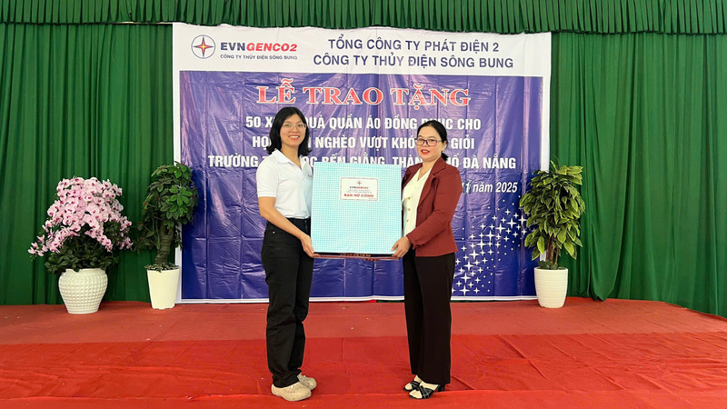 Bà Nguyễn Nho Bích Trâm, Trưởng Ban Nữ công Công ty Thủy điện Sông Bung (bìa trái) trao tặng quà của Ban Nữ công cho cô Kring Lưu, Hiệu trưởng Trường Tiểu học Bến Giằng (bìa phải), đại diện lãnh đạo nhà trường.