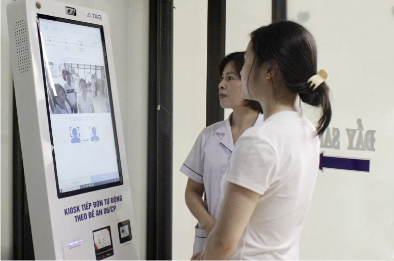 Nhân viên y tế hướng dẫn người dân sử dụng kiosk tiếp đón tự động, từng bước ứng dụng chuyển đổi số vào khám chữa bệnh tại tuyến cơ sở.