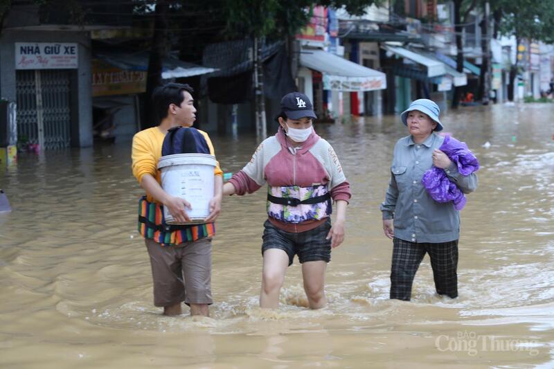 Người dân đeo phao ôm đồ sơ tán khỏi khu vực ngập úng.