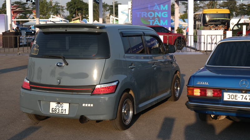 Một mẫu Subaru hatchback cỡ nhỏ với phong cách độ cá nhân hóa đỗ cạnh sedan cổ Mercedes-Benz 200, tạo nên sự tương phản giữa xe Nhật hiện đại và dòng xe Đức kinh điển tại không gian trưng bày của triển lãm.