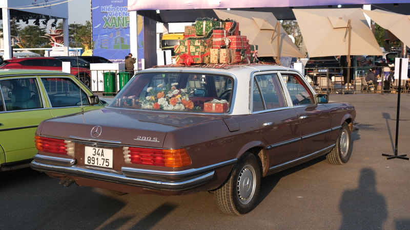 Mẫu Mercedes-Benz 280S cổ điển được trưng bày với phong cách trang trí hoài niệm, nổi bật bởi màu sơn nâu đặc trưng, nội thất bày hoa và hành lý trên nóc xe, gợi lại hình ảnh những chuyến du lịch châu Âu thập niên 1970–1980.
