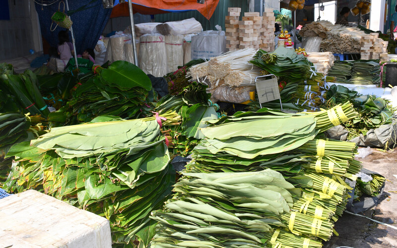 Tại phiên chợ, lá dong được bày bán thành từng bó lớn, xanh mướt, xếp gọn gàng trên vỉa hè. Nguồn lá chủ yếu được thu mua từ khu vực Gia Kiệm (Đồng Nai), khu vực Bảo Lộc (Lâm Đồng), xã Bà Điểm (TP. Hồ Chí Minh). Ảnh: Thanh Minh