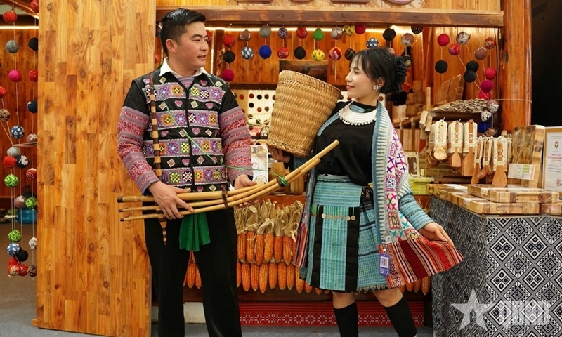 Chị Lường Thị Thắm và anh Vàng A Xìn trong trang phục truyền thống dân tộc Mông, thể hiện điệu múa và tiếng khèn tại gian hàng Hội chợ Mùa Xuân 2026. Ảnh: QĐND