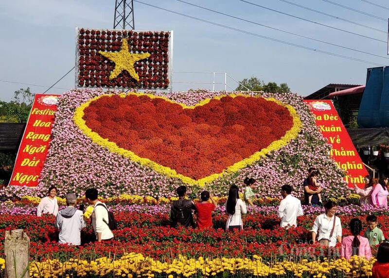 Du khách check-in tại tiểu cảnh lá cờ và trái tim được ghép từ các loài hoa, điểm nhấn thu hút khách tại Tổ hợp tác Tân An.