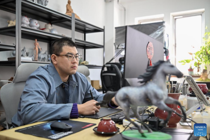 Nghệ sĩ đang sáng tác bằng bút điện tử trên máy tính tại Văn phòng chế tác tượng đất sét. Ảnh: Xinhua
