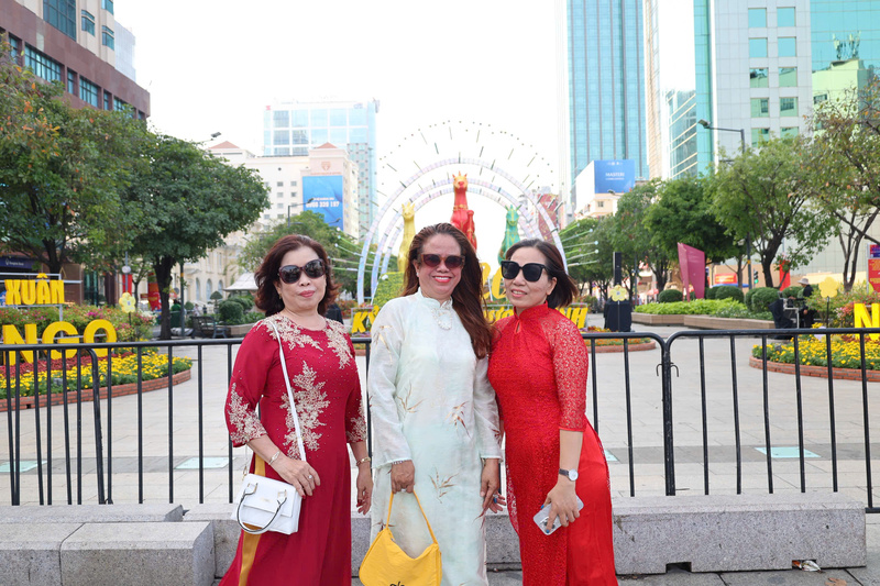 Du khách xúng xính trong tà áo dài rực rỡ, khoe sắc bên ngoài hàng rào Đường hoa Nguyễn Huệ trong chiều 28 Tết. Ảnh: Minh Anh.