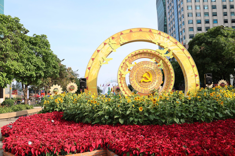 Đại cảnh trang trí với biểu tượng trống đồng và búa liềm vàng rực rỡ trên nền hoa hướng dương, thể hiện tinh thần truyền thống và niềm tự hào dân tộc. Ảnh: Minh Anh.