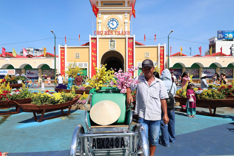 Nụ cười đôn hậu của chú Ba Tâm (62 tuổi) bên chiếc xích lô được trang trí hoa xuân, sẵn sàng phục vụ du khách trải nghiệm không khí Tết tại trung tâm thành phố. Ảnh: Minh Anh.