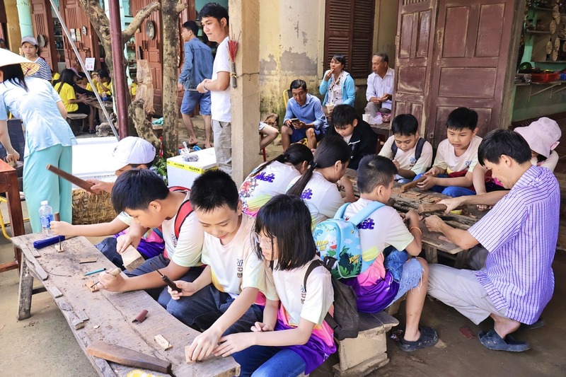 Em Huỳnh Văn Tâm, học sinh Trường Tiểu học Trần Cao Vân chia sẻ: “Chúng em được các anh chị giới thiệu về sản phẩm tại làng nghề, được cầm tay hướng dẫn khắc tên mình lên gỗ, rất là vui. Sau khi về chúng em sẽ viết lại những cảm nhận và bài học của mình để lưu lại làm kỷ niệm”. Ảnh: Diễm Phúc