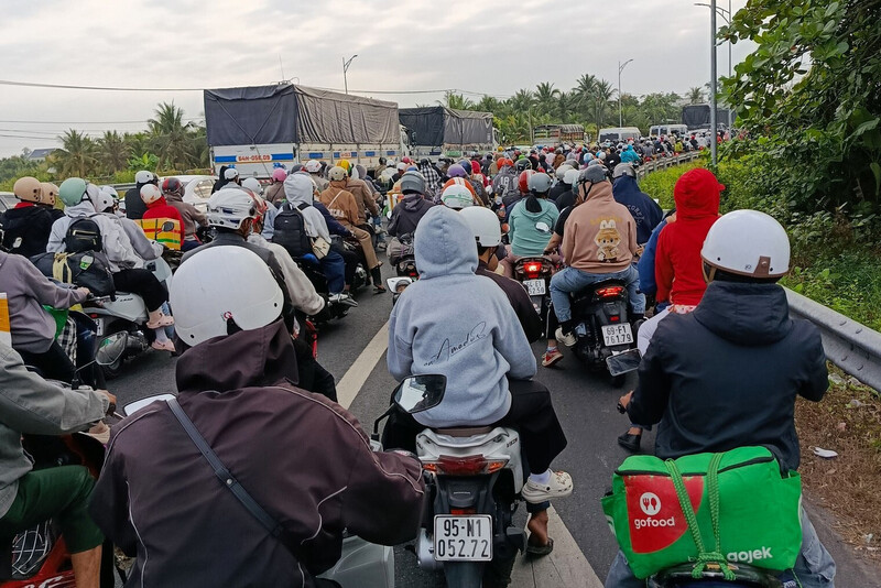 Người dân mặc áo khoác, trùm kín người di chuyển trong dòng xe đông đúc dưới bầu trời nhiều mây.