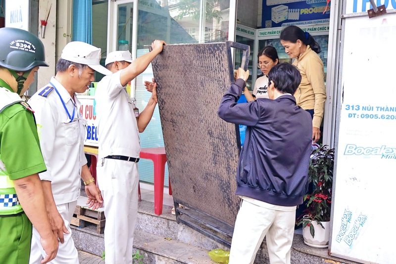 Các lực lượng cùng hỗ trợ người dân di dời các biển hiệu, chậu cây, bục sắt để trả lại không gian cho vỉa hè. Ảnh: Diễm Phúc