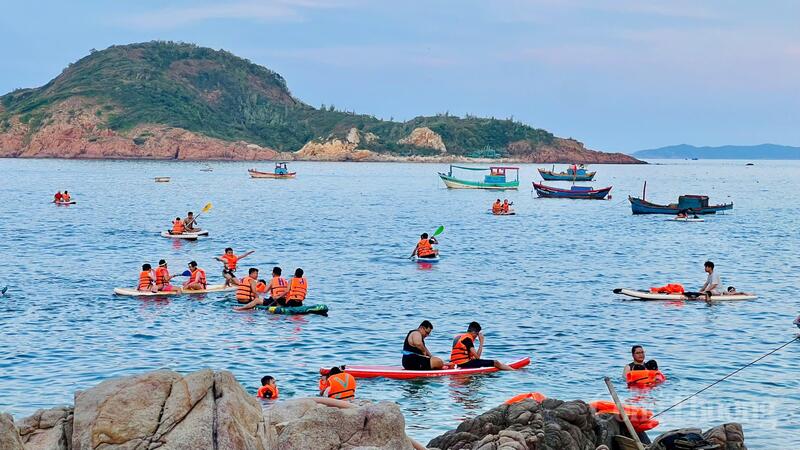 Mặt trời dần khuất sau núi, ánh nắng nhuộm vàng mặt biển. Bãi cát trắng trở nên đông đúc khi du khách từ nhiều nơi đổ về.