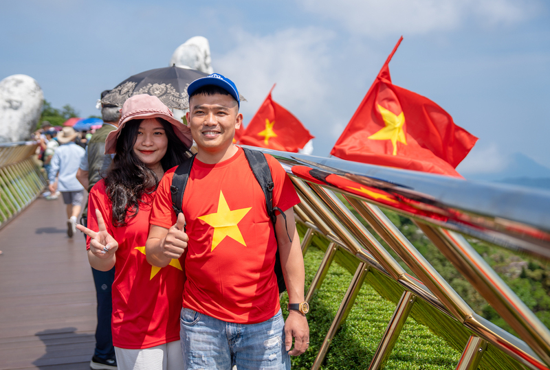 Các du khách trong màu áo cờ đỏ sao vàng check in cùng cờ Tổ quốc tại Cầu Vàng. Ảnh: Bình An
