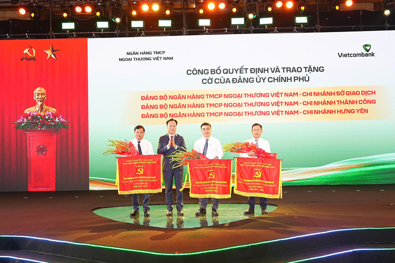 Đại diện Đảng ủy Chính phủ trao cờ và tặng hoa cho đại diện 03 Đảng bộ trực thuộc Vietcombank được công nhận đạt tiêu chuẩn hoàn thành xuất sắc nhiệm vụ tiêu biểu giai đoạn 2021 - 2025. Ảnh: DNCC