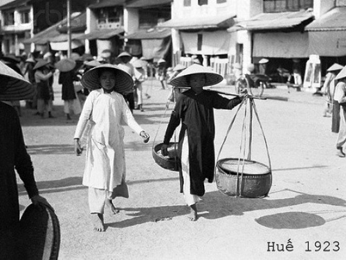 Một khu chợ ở Huế năm 1923 (Ảnh: Bettmann/CORBIS). Các bà, các cô khi đó thường mặc áo dài không chiết eo, đội nón lá, đi chân đất. Chiếc quần trong bộ áo dài kiểu cổ này cũng được cắt khá cao để thuận tiện cho việc đi lại.